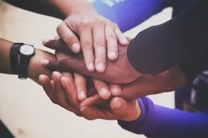 a pile of multiracial hands come together symbolizing teamwork