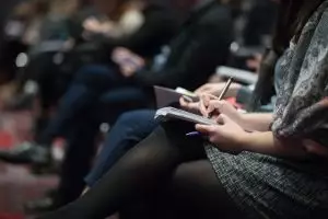 many people sitting in a row writing in their individual notebooks