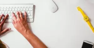 hands on keyboard on left hand side of image with watch and computer mouse on the right hand side of the image