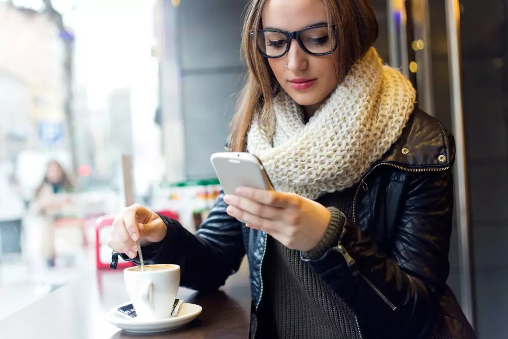 Women at coffee shop drinking coffee and looking at phone.