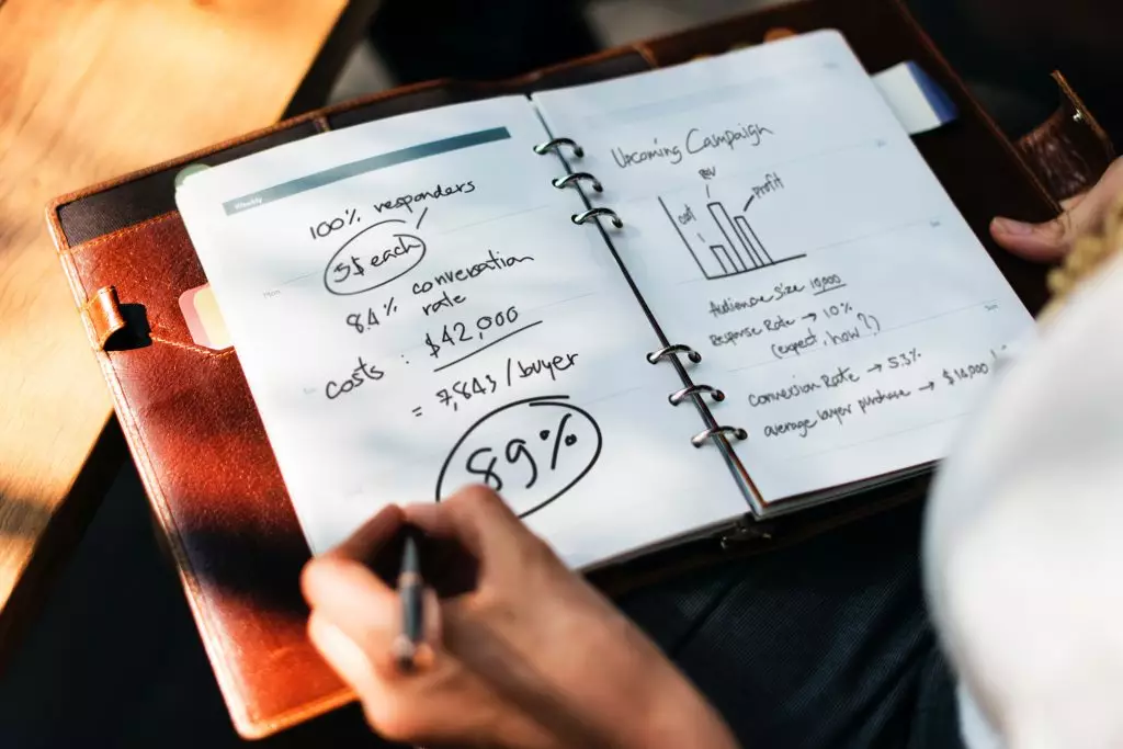 Open notebook with a woman's hand making notes in black ink.