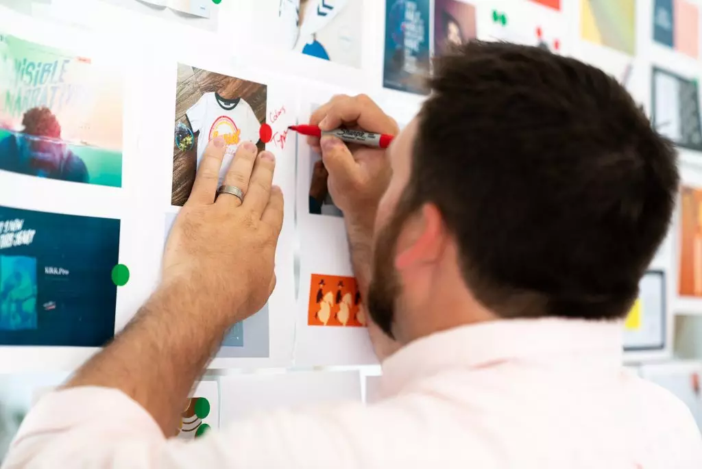 A male Oneupweb employee writing notes on a collage of graphic design styles.