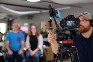 A male videographer prepares to film a man and woman for a YouTube video.