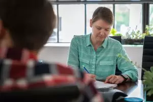 A female account manager writing in her notebook during a meeting