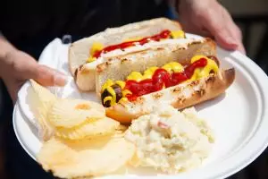 two hot dogs on buns with chips and potato salad on paper plate