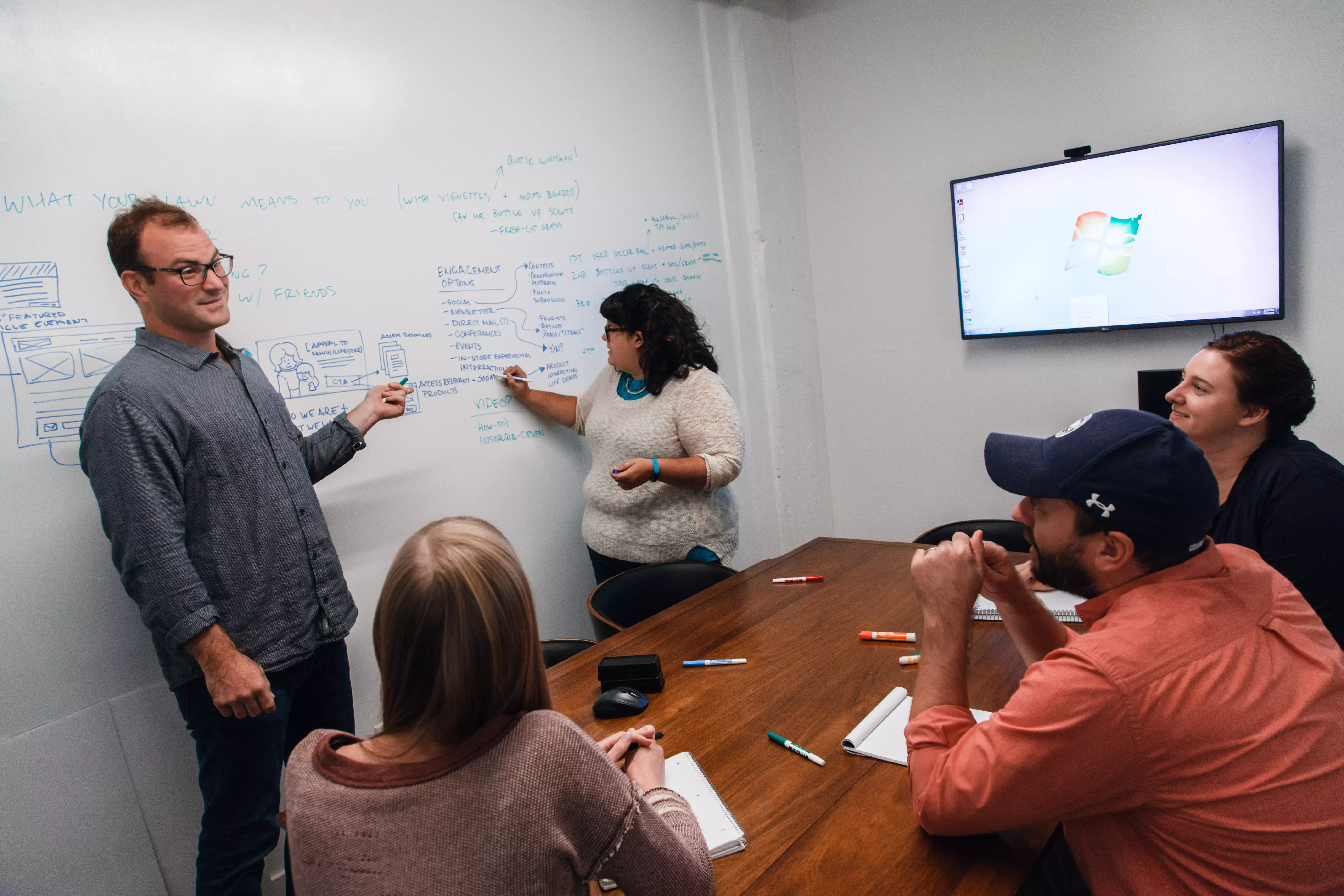 five people in a conference room with two standing and three sitting