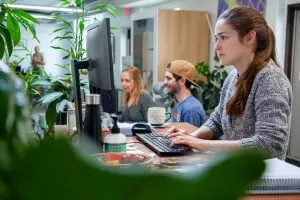 woman in ponytail sitting at computer with two colleagues behind her