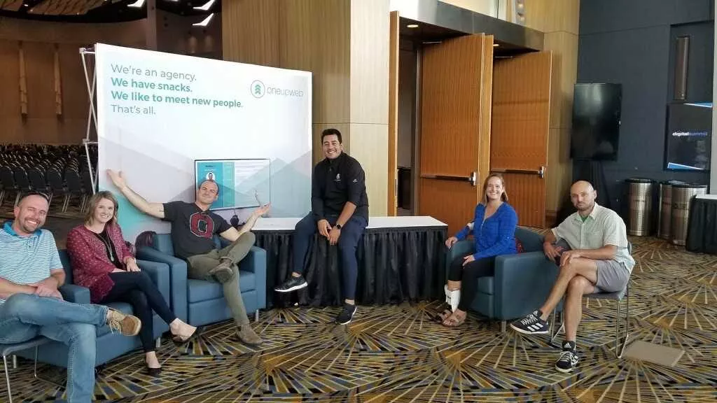 group of people sitting in front of oneupweb sign at conference booth