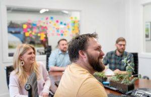 Marketing professionals gather around a meeting table and laugh together