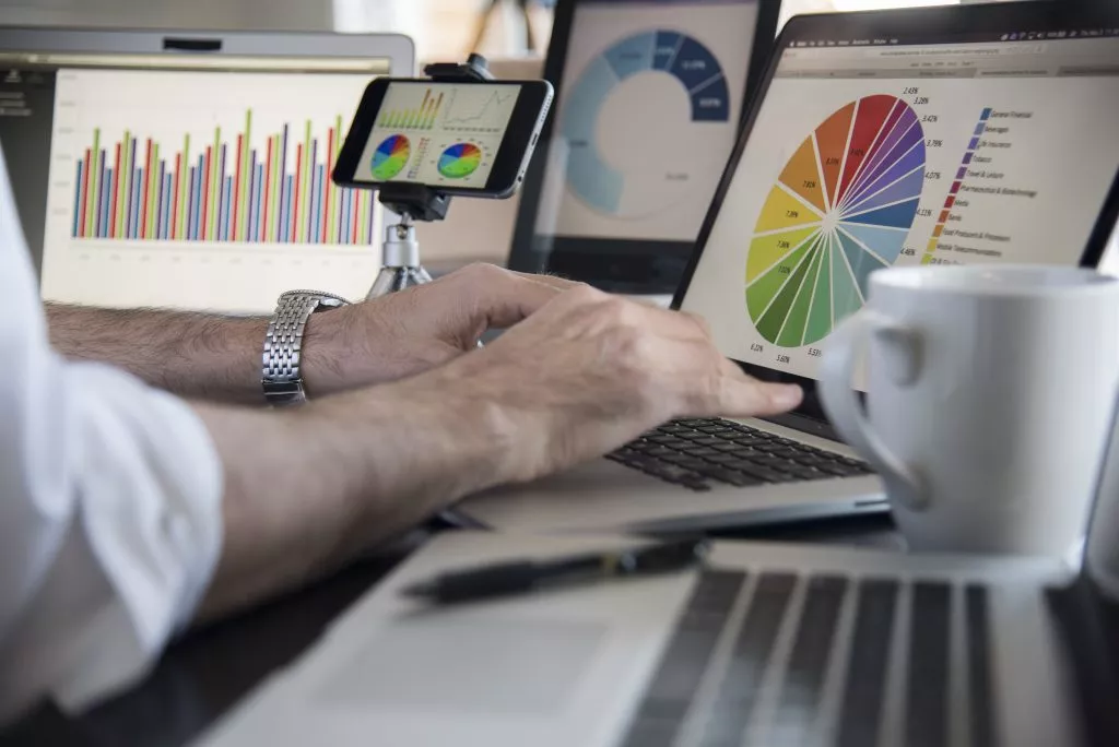 a mans hands rest on a computer keyboard while various devices show pie charts, bar graphs and other data to analyze