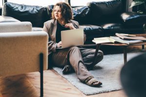 Caucasian woman sitting on carpet dressed in business attire with laptop in her lap