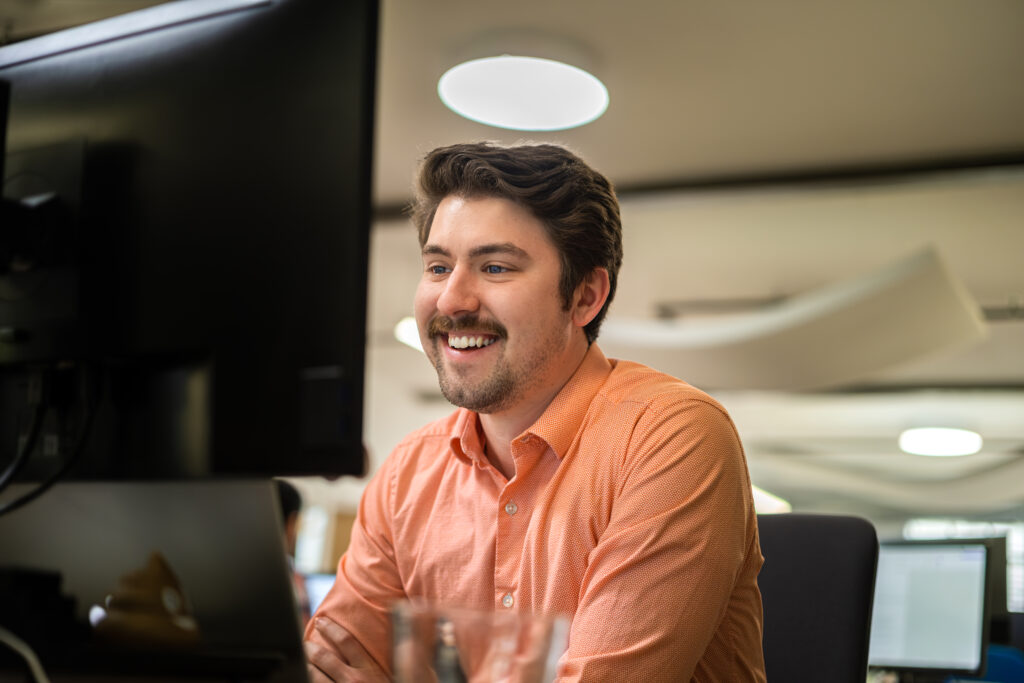 a marketing professional working at his computer in an office setting while smiling