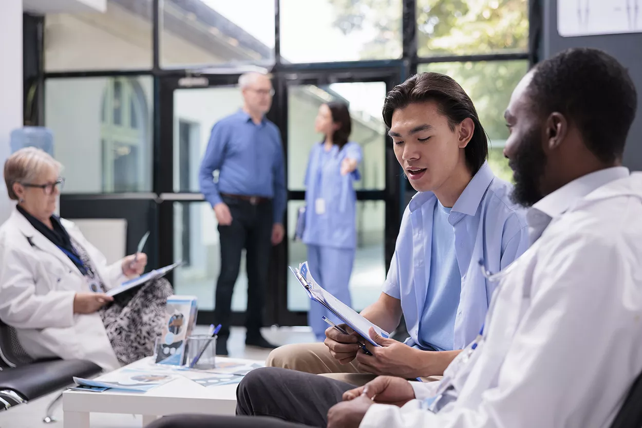 Asian patient holding clipboard filling medical report while discussing health care treatment with specialist medic