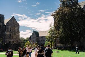 Students walk between buildings on a beautiful university campus.